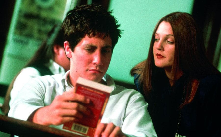 Jake Gyllenhaal holding a book while Drew Barrymore looks over his shoulder 