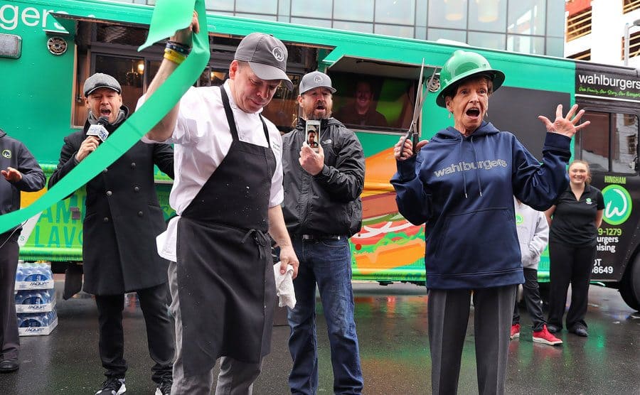 Donnie, Paul, Bob, and Alma Wahlberg holding a ribbon-cutting ceremony with a Wahlburgers truck behind them 