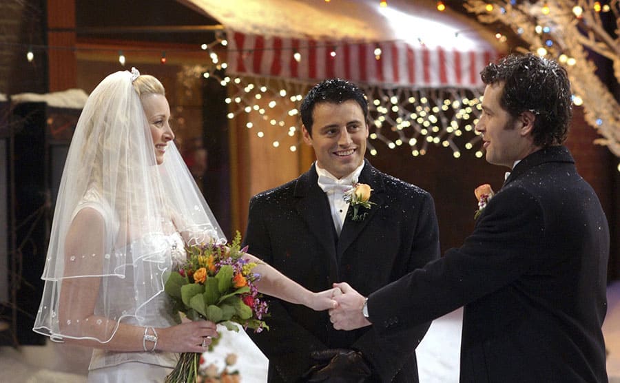Lisa Kudrow and Paul Rudd holding hands standing across from each other on their wedding day with Matt LeBlanc initiating the ceremony 