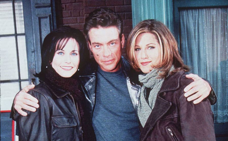 Courteney Cox, Jean-Claude Van Damme, and Jennifer Aniston on the set of Friends posing for a photograph 