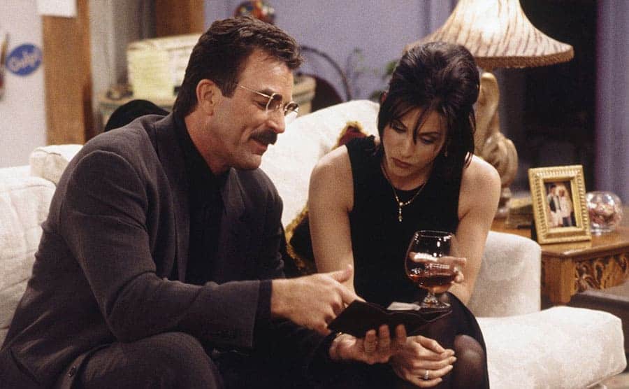 Tom Selleck showing Courteney Cox something on his phone while they are on a date 