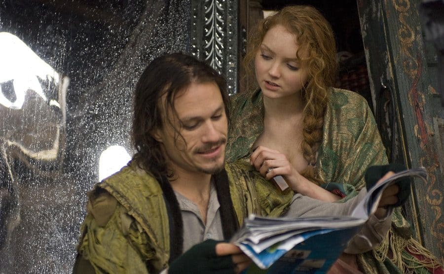 Heath Ledger reading a paper while Lily Cole sits behind him talking to him 