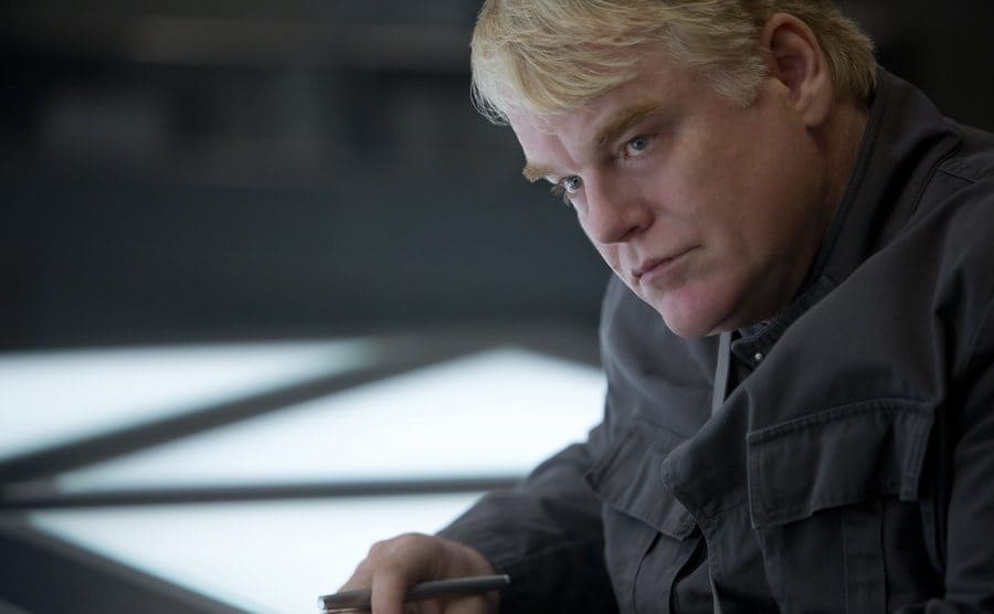 Philip Seymour Hoffman sitting at a table in The Hunger Games 