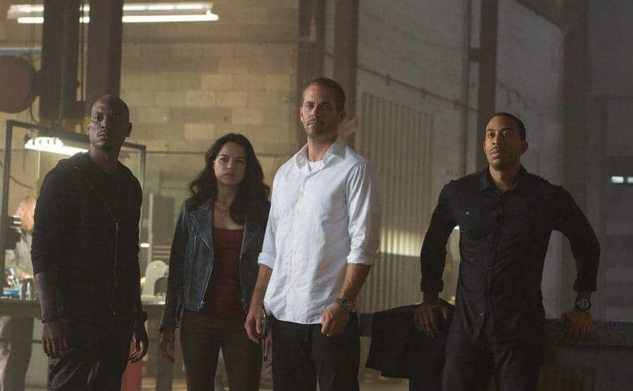 Tyrese Gibson, Michelle Rodriguez, Paul Walker, and Ludacris standing in a garage 