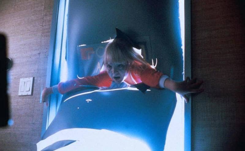 Heather O'Rourke holding herself on a doorframe while someone tries to pull her through 