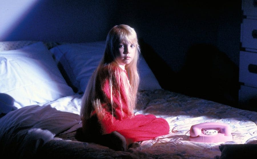 Heather O'Rourke sitting on a bed with a pink telephone next to her 