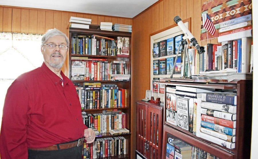 Tom Carey is standing in a room filled with books. 