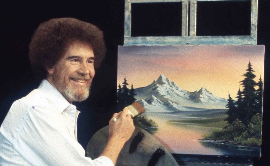 Bob Ross sitting in front of an easel 