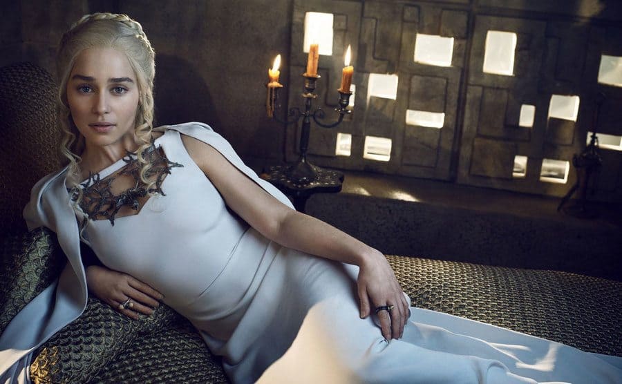 Emilia Clarke as Khaleesi lying on a small loveseat 