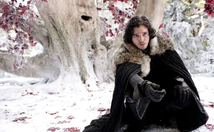 Kit Harington kneeling in the snow, reaching his arm out in a scene from Game of Thrones 