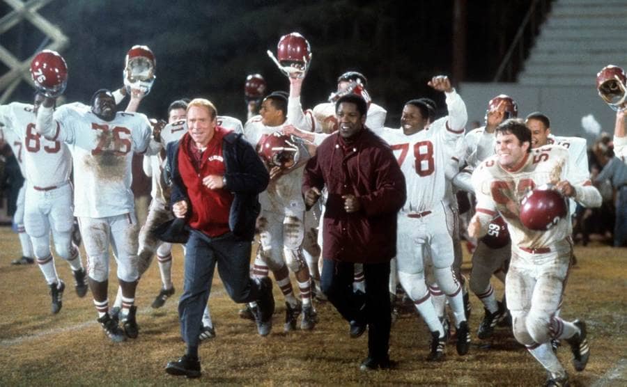 Will Patton and Denzel Washington run out onto the field in a scene from the film 'Remember The Titans', 2000.