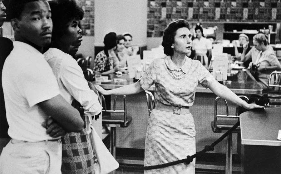 A Caucasian woman hurriedly bars the way as Negroes were about to enter the lunch counter of this downtown department store.