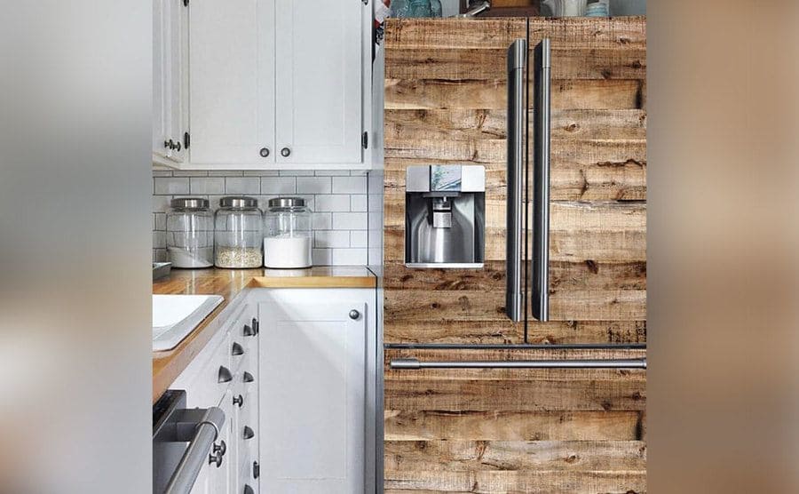A stainless steel kitchen fridge covered in wood-like tapestry to give it a different look.