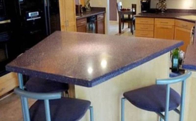 A trapezoid-shaped island in the middle of the kitchen with three bar stools placed around it. 