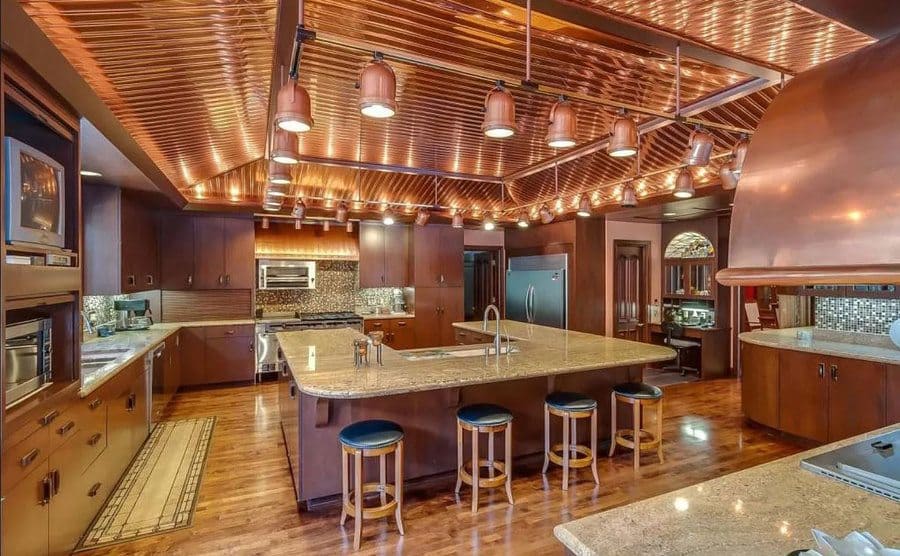 A large kitchen with a copper lighting rig hanging from the ceiling above the island in the center. 