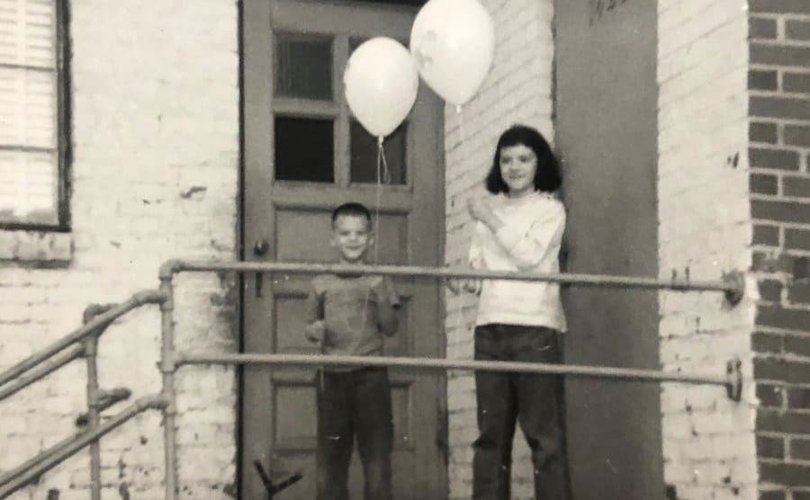 Nelson and Cook on their front steps holding balloons. 