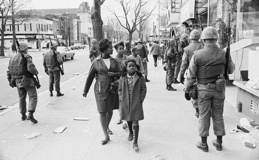 An African American woman walking past soldiers on the streets of DC during the riots. 