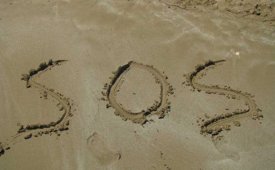 The word 'sos' is written in the sand on the beach.