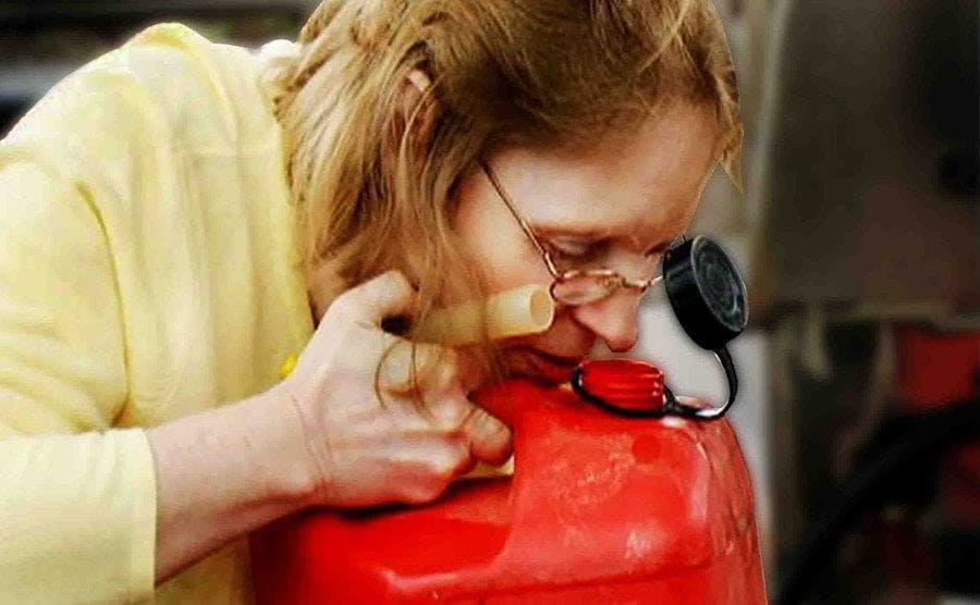 Theresa is sniffing gasoline out of a large jug. 