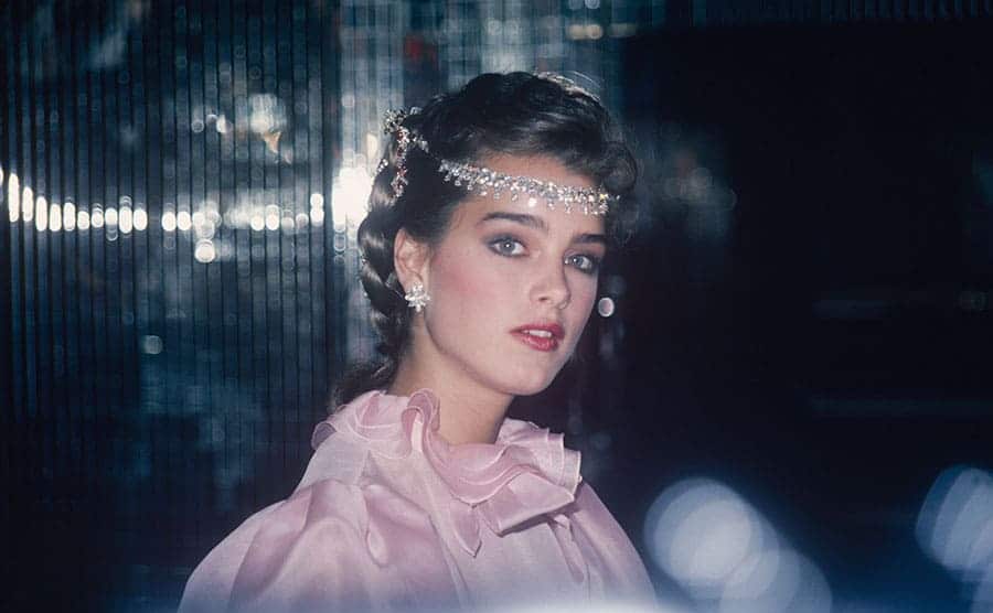 Brooke Shields posing in a pink ruffled dress with a jeweled headpiece 