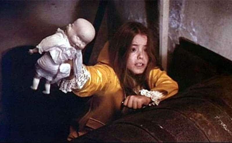Brooke Shields holding a doll up while looking scared 