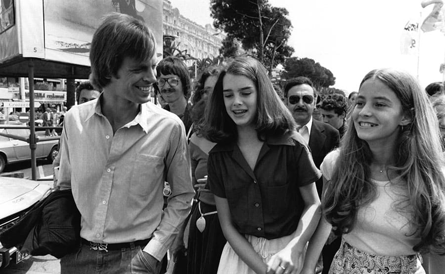 Keith Carradine, Brooke Shields, and her sister walking through the street with a large crowd behind them 