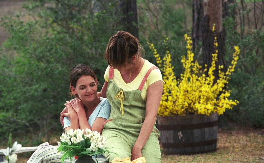 Katie Holmes and Nina Rapeta sitting in the woods with a large yellow potted plant behind them