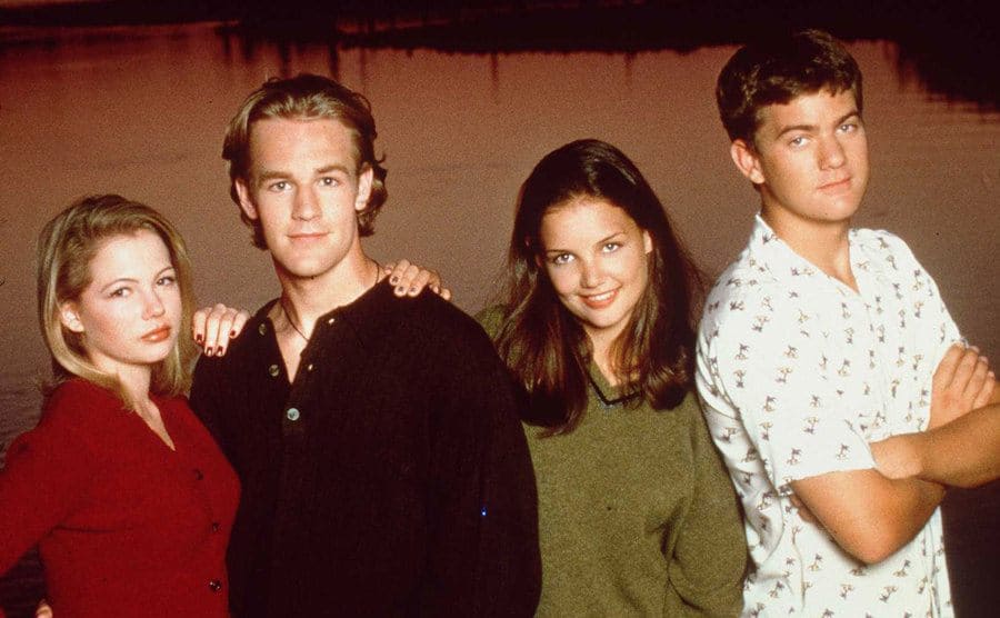 Michelle Williams, James Van Der Beek, Katie Holmes, and Joshua Jackson posing together in front of a lake at dusk 