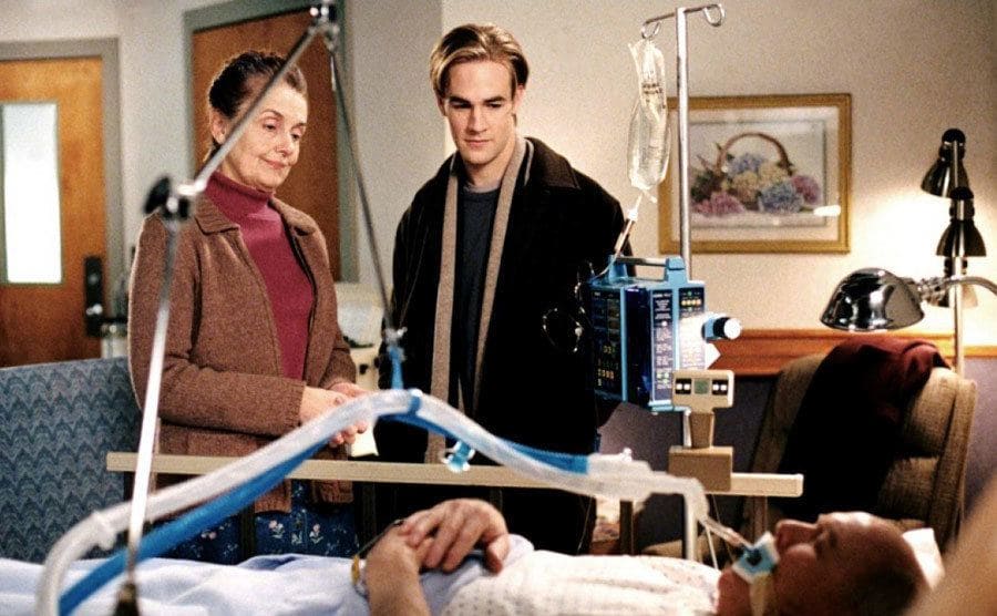 Mary Beth Peil and James Van der Beek in a hospital standing next to a bed with a man on a breathing tube 