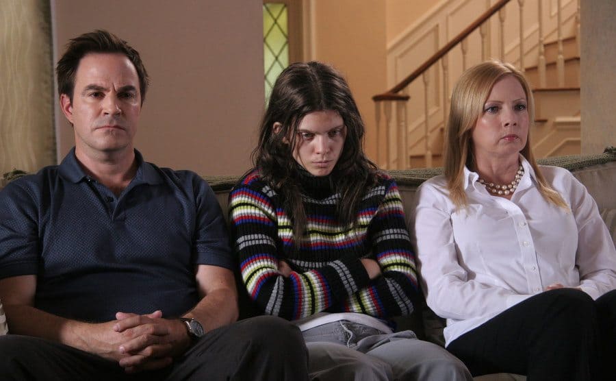 Roger Bart, AnnaLynne McCord, and Traci Lords sitting on a couch looking serious in a scene from Excision 