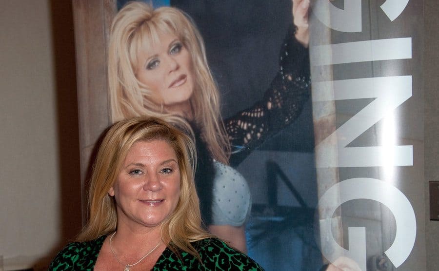 Ginger Lynn posing in front of an old poster of herself 
