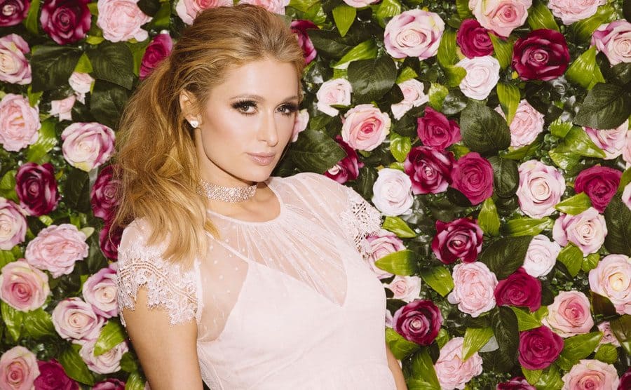 Paris Hilton posing in front of a wall of roses 
