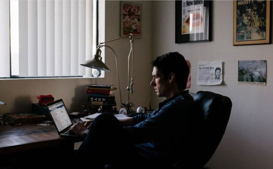 Jensen is sitting at his desk using social media on his computer. 