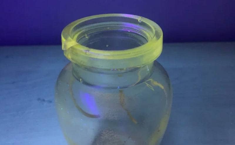 A small cracked jar that looks like a small vase. The jar is glowing yellow-green under UV light. 