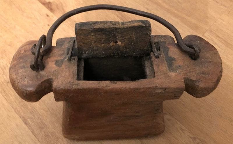 An old box with a wooden and rusty opening. Along with a metal handle used for lifting. 