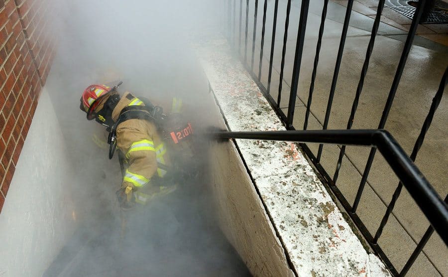 A firefighter is going down into the smoke coming from a basement fire. 