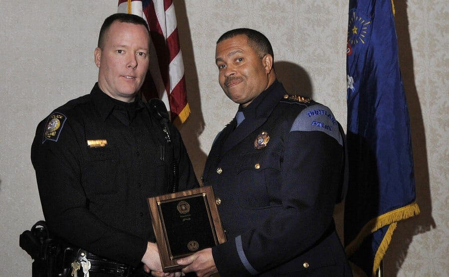 A police officer is receiving a plaque in honor of his bravery and hard work from his commanding officer. 