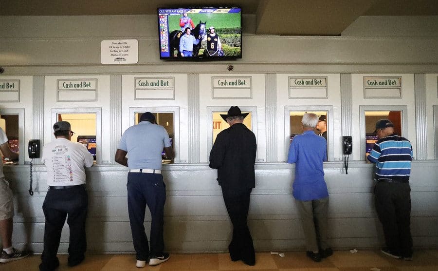 Gamblers stand at betting windows at the racetrack. 
