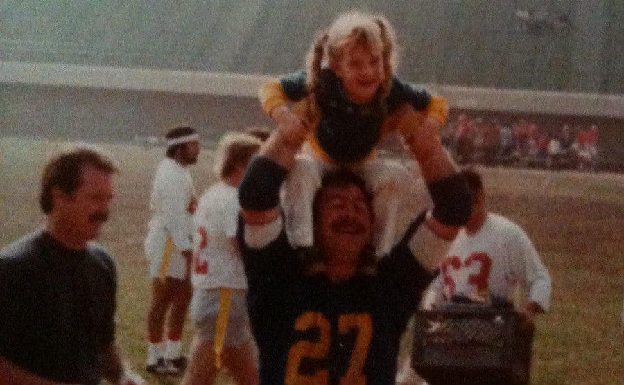 Adair on the football field lifting his little girl over his head. 