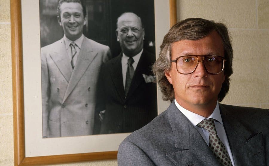 A photo of Maurizio Gucci posing in front of a photo of his father. 