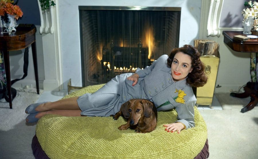Joan Crawford lying in front of her fireplace with her pet dachshund circa 1940 