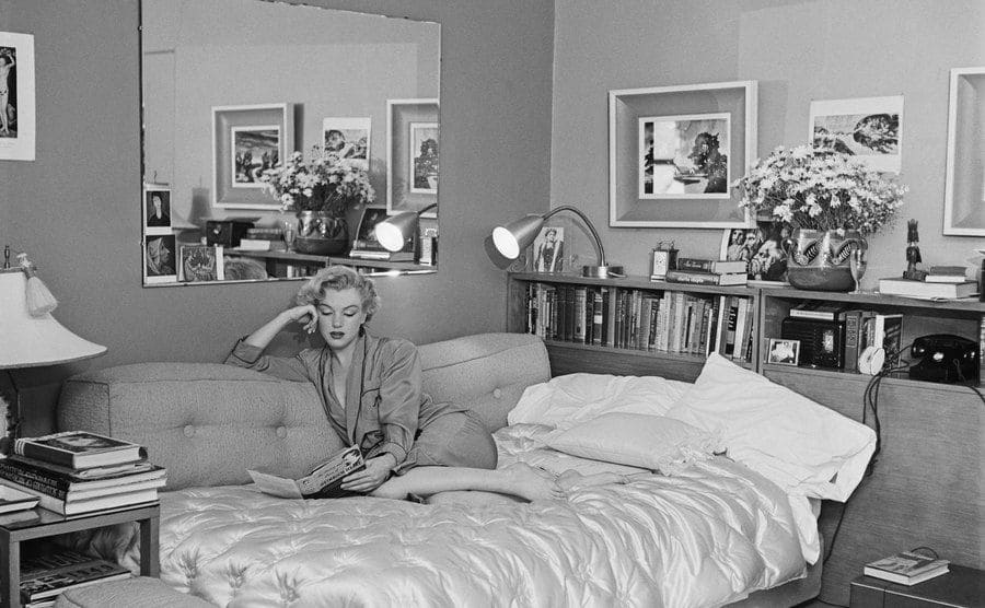 Marilyn Monroe sitting in her sofa bed reading a magazine 