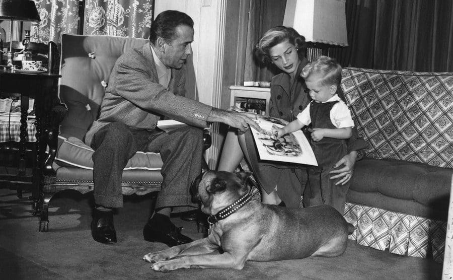 Humphrey Bogart and Lauren Bacall at home with their son and dog reading a book to him 