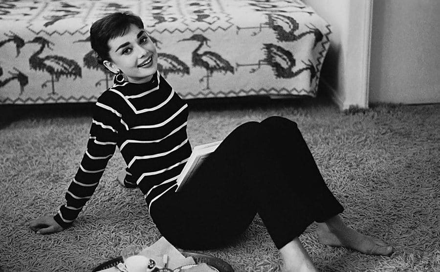Audrey Hepburn sitting in her living room with a sofa bed behind her 