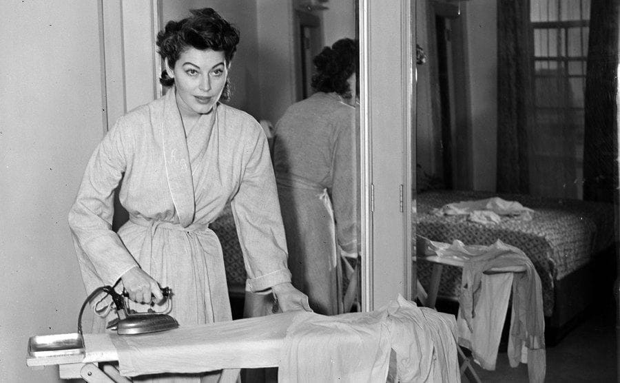 Ava Gardner ironing in her pajamas at home 
