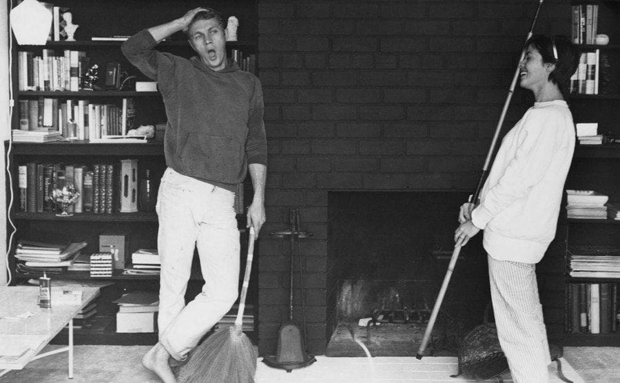Steve McQueen and his wife standing around the fireplace while doing chores 