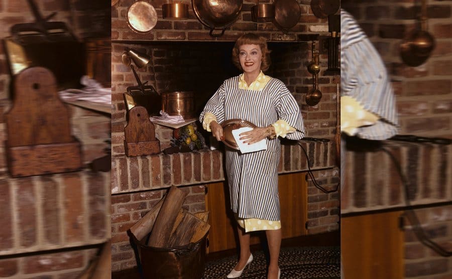 Bette Davis in her kitchen drying the lid to a copper pot 