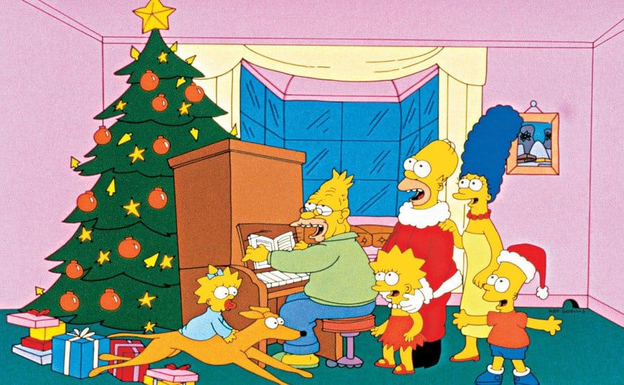 A scene of the Simpsons around the Christmas tree while Homer’s dad plays the piano.