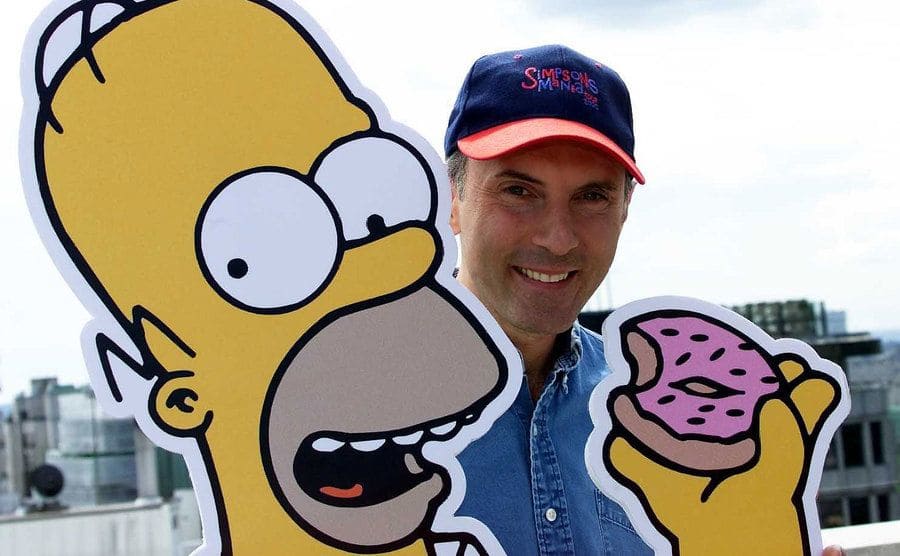 Dan Castellaneta is posing with a cut-out of Homer Simpson. 
