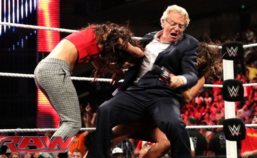 Jerry Springer as the host of WWE Raw with two women taking him down in a wrestling move 